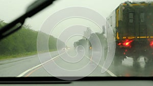 Column of modern military vehicles on the highway. Defocussed traffic viewed through a car windscreen covered in rain This is in