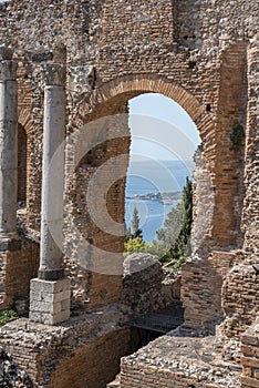 Columns and arch at old ruins of ancient Greek theater with sea in background