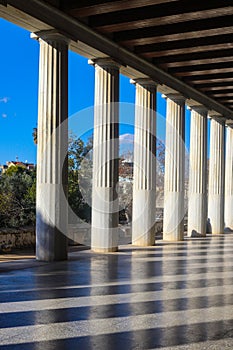 Columns cast shadows across the marble floor of the covered walkway at the restored 2nd century BC Stoa of Attalos in the ancient