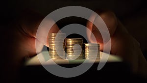 Columns of coins grow against the background of hands using a smartphone in the dark. CG