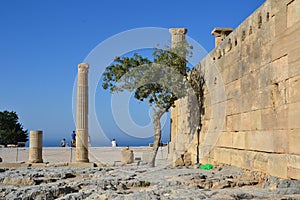 Columns on the hellenistic stoa of the Acropolis of Lindos, Rhodes, Greece, Blue sky, olive tree and beatiful sea view in the back