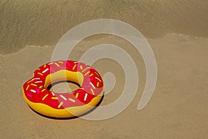 Colurful inflatable donut on the seashore. with soft wave of blue ocean in outdoor sun lighting on sandy beach.