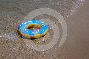 Colurful inflatable donut on the seashore. with soft wave of blue ocean in outdoor sun lighting on sandy beach.