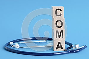 Coma word written on wooden blocks and stethoscope on light blue background