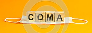 Coma the word is written on wooden cubes lying on a medical mask. Concept. yellow background