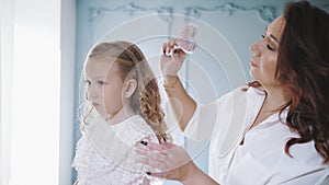 comb child hair. mom is combing her little daughter's hair, doing her hair. woman and little girl stand in front of the