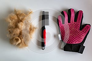 Comb and glove for combing wool and tangles in cats next to a pile of wool.