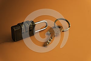 Combination padlock and key isolated on orange background.