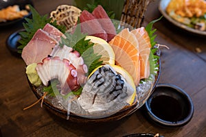 Combination sashimi set consisting of pickled saba, salmon, squid, tuna and hamachi on a dark bowl