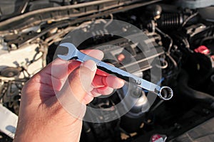 Combination wrench or open end spanner chrome in a car mechanic hand with engine compartment blurred on background