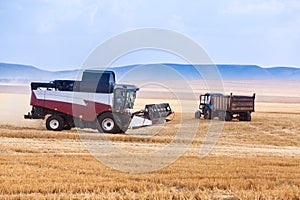 A combine harvester drives through an agricultural field past a tractor with a trailer