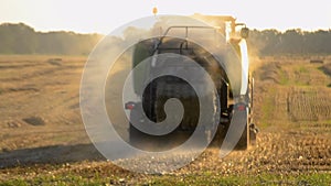 Combine harvester pressing straw field bales driving across field sunny summer