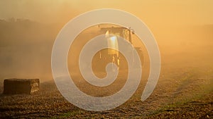 Combine harvester pressing straw field bales driving across field sunny summer