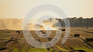 Combine harvester pressing straw field bales driving across field sunny summer