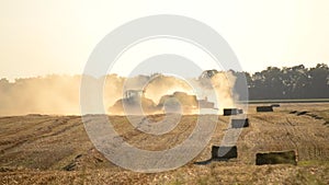 Combine harvester pressing straw field bales driving across field sunny summer