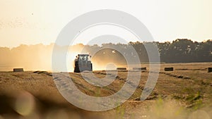 Combine harvester pressing straw field bales driving across field sunny summer