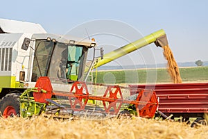 Combine harvester unloading wheat grains into tractor trailer.