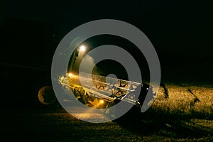 Combine harvester working in a wheat field at night with lights