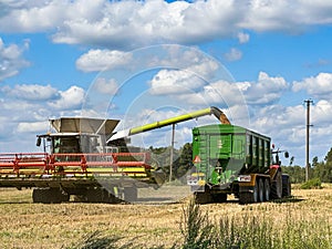 Combine harvesting grain by pouring in tracktor trailer in a sunny day. Agriculture business