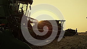 Combine silhouette at golden sunset farmland. Seasonal grain harvesting time.