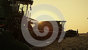 Combine silhouette at golden sunset farmland. Seasonal grain harvesting time.