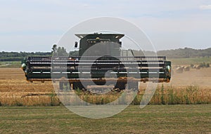 Combine Tractor Coming Straight on Harvesting Ripe Wheat in a Field with Dust Flying through the Air