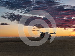 Combine working after sunset to harvest corn in the fall