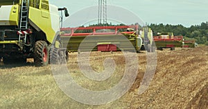 Combines go in a row after harvest. End of harvest. Rear view. Modern combine claas harvesting rape field. Harvesting