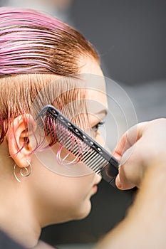 Combing the hair of a young woman during coloring hair in pink color at a hair salon close up.