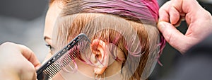 Combing the hair of a young woman during coloring hair in pink color at a hair salon close up.