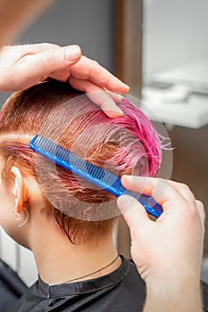 Combing the hair of a young woman during coloring hair in pink color at a hair salon close up.