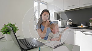 Combining work and parenting, mother with crying little son while working on laptop computer and talking on mobile phone