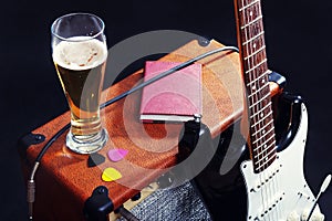 Combo for electric guitar with black guitar, glass of beer and notepad on black background