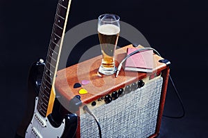 Combo for guitar with black guitar, glass of beer and notepad on black background