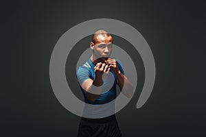 Come closer. Muscular boxer is ready to fight. Young sportsman standing over dark background