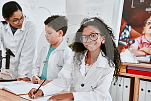 Come join in on the fun. Portrait of an adorable young school girl writing notes in science class with her teacher and