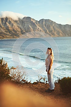 Come join me down here. Full length shot of an attractive young woman standing alone on a mountainside near the sea