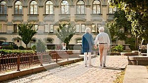 Come with me. Back view of elderly couple holding hands while walking together outdoors