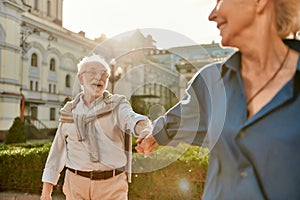 Come with me. Beautiful and happy elderly couple holding hands and smiling while spending time together outdoors on a