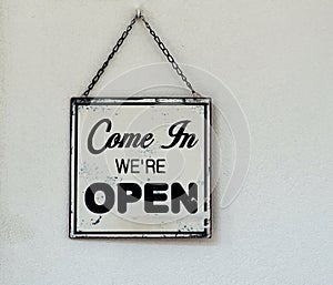 Come in we are open, black and white retro sign on white wall of a store.