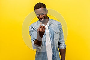 Come to me. Portrait of handsome man making beckoning gesture and smiling. indoor studio shot isolated on yellow background