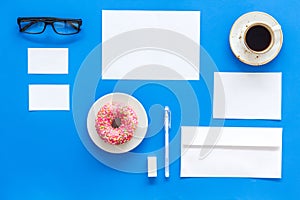 Come up with brand identity. Blank stationery for branding near coffee and donut on blue background top view mockup