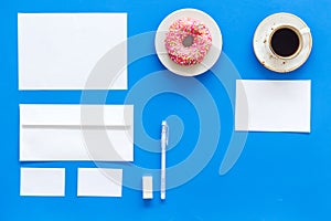 Come up with brand identity. Blank stationery for branding near coffee and donut on blue background top view mockup