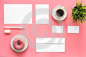 Come up with brand identity. Blank stationery for branding near coffee and donut on pink background top view mockup