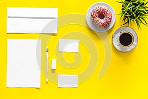 Come up with brand identity. Blank stationery for branding near coffee and donut on yellow background top view mockup