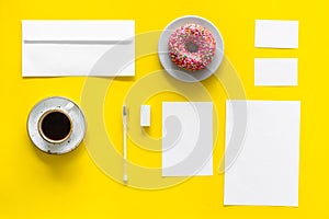 Come up with brand identity. Blank stationery for branding near coffee and donut on yellow background top view mockup