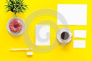 Come up with brand identity. Blank stationery for branding near coffee and donut on yellow background top view mockup
