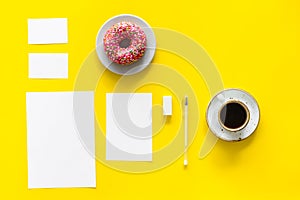 Come up with brand identity. Blank stationery for branding near coffee and donut on yellow background top view mockup