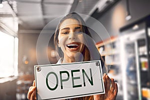 Come on in Were open. Cropped portrait of an attractive young woman holding up an open sign while standing in her coffee