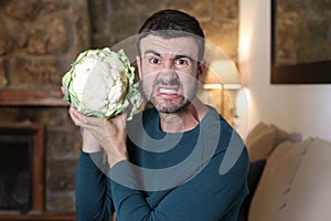 Comedic image of man disliking a raw cauliflower